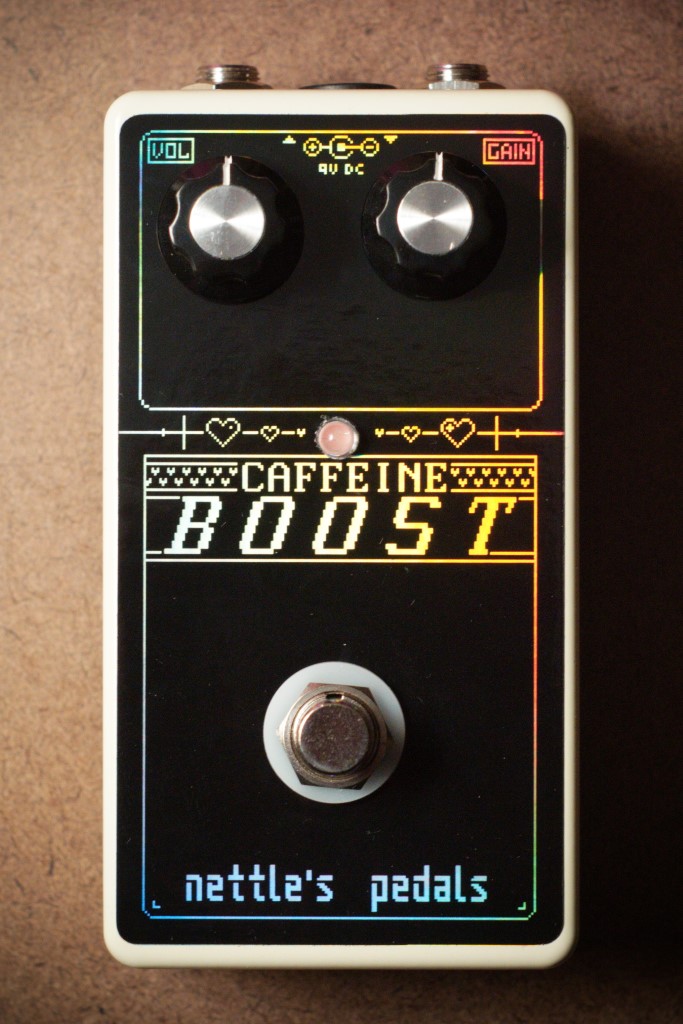 photograph of Caffiene Boost pedal. It is cream colored with a black and holographic logo and has two knobs labeled 'vol' and 'gain'